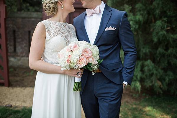 details of the bridal gown and bouquet with pink roses and white hydrangea. The pink roses match the grooms pink bowtie.
